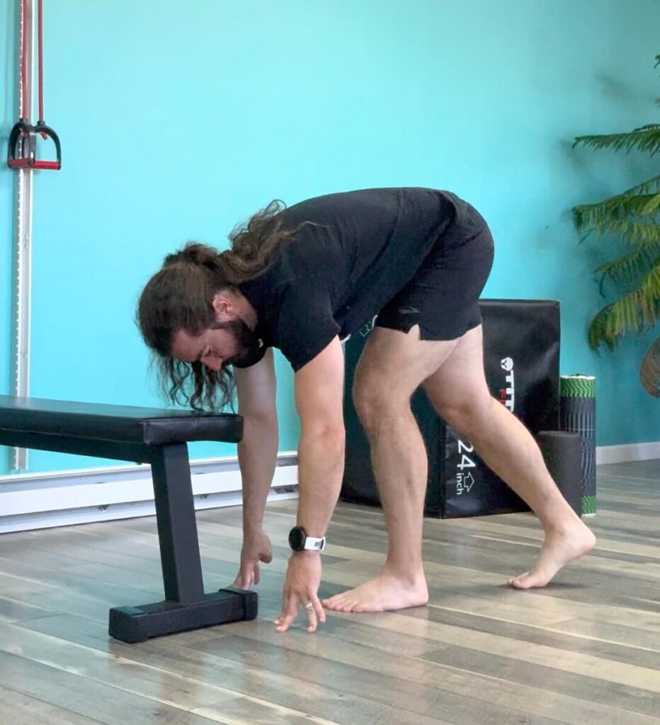 Dr. John in a split stance with his left leg in front hands touching the floor infront of him doing a dynamic hamstring stretch. This is one of 3 exercises to help heal your hamstring strain fast